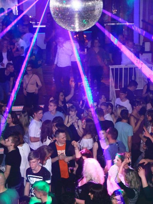 Tanzende Menschen in einem Club mit violetter Beleuchtung. 