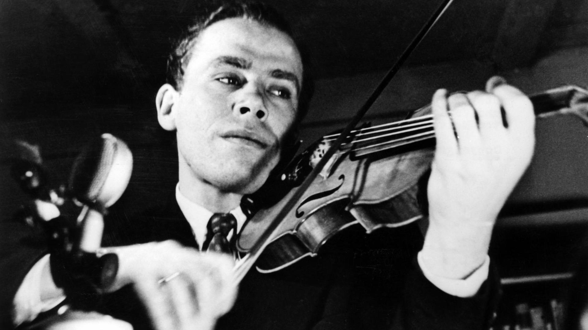 Schwarz-Weiß-Foto mit Helmut Zacharias als jüngerem Mann. Er trägt einen Anzug mit weißem Hemd und Schlips und spielt Geige.