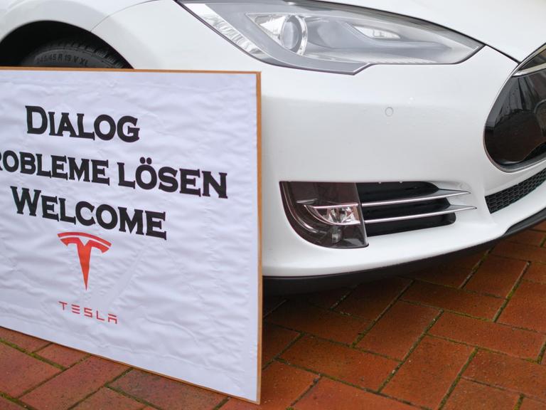 Ein Schild mit der Aufschrift "Dialog Probleme Lösen Welcome Tesla" steht an einem Elektrofahrzeug der Marke Tesla am Rande einer Kundgebung von Anwohnern, die sich für den Bau der geplanten Tesla-Fabrik einsetzen.