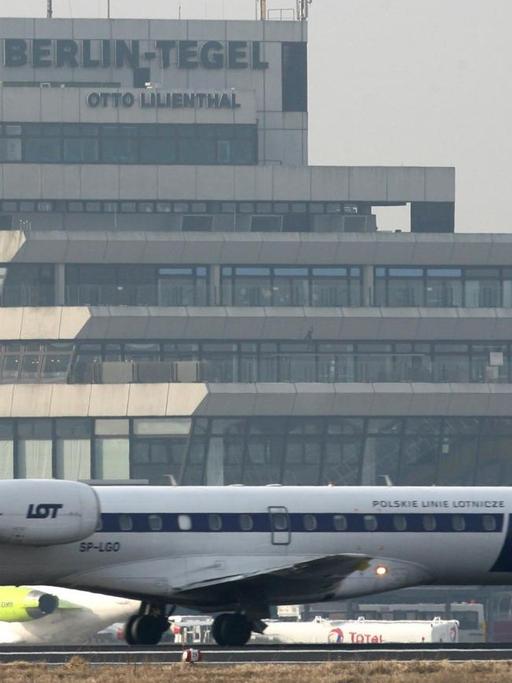 Ein Verkehrsflugzeug der polnischen Fluggesellschaft Lot steht auf dem Flughafen Berlin Tegel. Im Hintergrund sieht man den Tower und das Flughafengebäude.