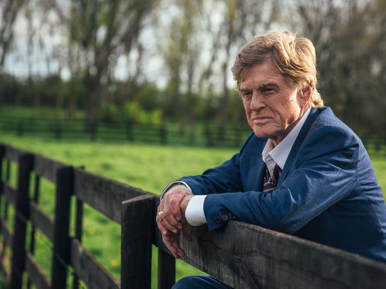 Der Schauspieler Robert Redford steht an einem Zaun und schaut in die Ferne.