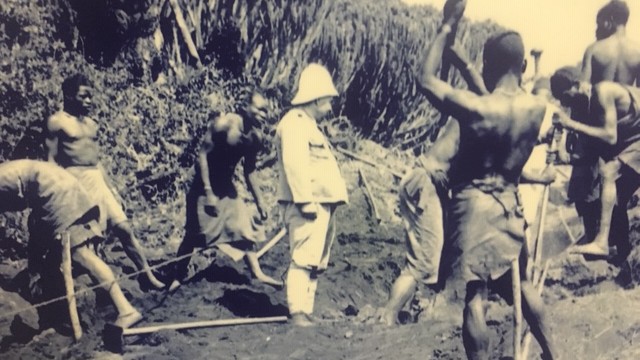 Europäer in Uniform beaufsichtigt afrikanische Landarbeiter