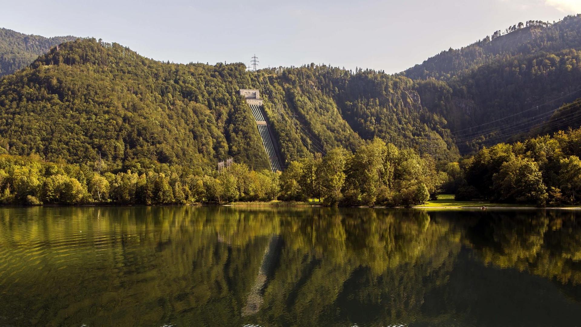 Ansicht des Walchensee-Kraftwerks direkt am See zwischen bewaldeten Hügeln gelegen.