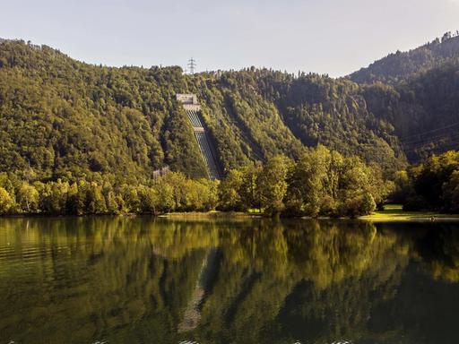 Ansicht des Walchensee-Kraftwerks direkt am See zwischen bewaldeten Hügeln gelegen.