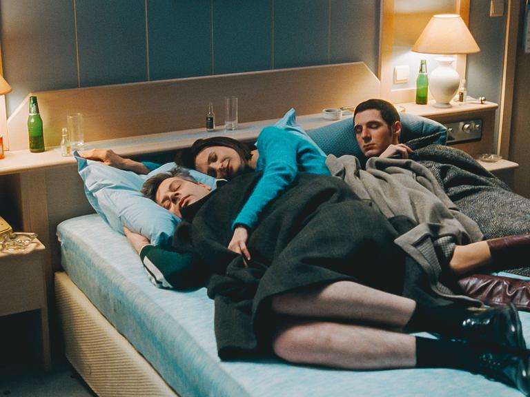 Eine Frau liegt zwischen zwei Männern in einem Hotelbett: Szene aus dem Film "Zimmer 212 – In einer magischen Nacht".