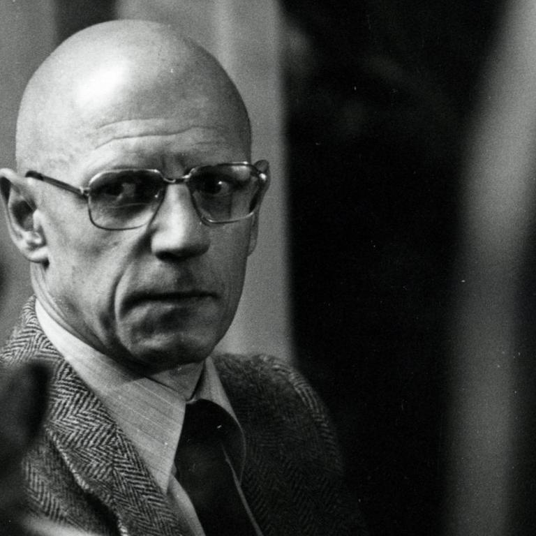Der französische Philosoph Michel Foucault schaut aus den Augenwinkel an der Kamera vorbei. Er trägt eine große Brille.