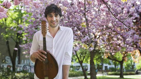 Der Musiker Avi Avital mit einer Mandoline vor einem blühenden Baum
