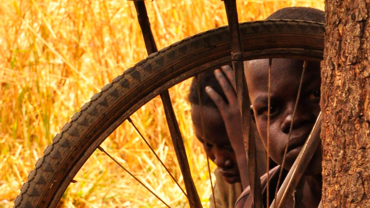 Ein Kind schaut hinter einem Fahrradreifen hindurch 