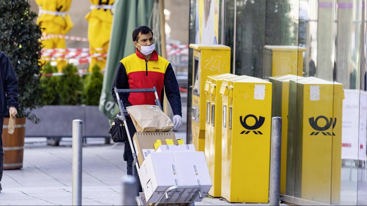 Ein DHL-Mitarbeiter mit Mund-Nase-Schutz liefert in Stuttgart Pakete aus.