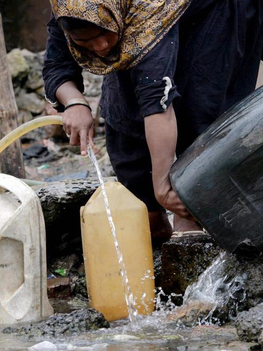 Eine pakistanische Frau füllt Gefäße mit Trinkwasser an einem Brunnen.