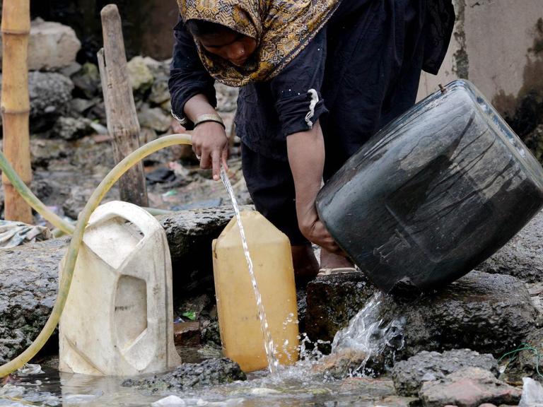 Eine pakistanische Frau füllt Gefäße mit Trinkwasser an einem Brunnen.