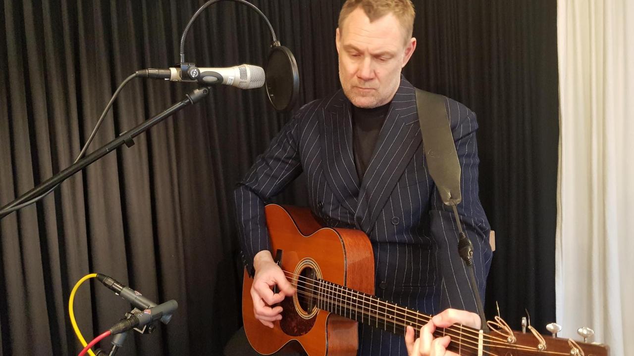 David Gray steht mit Gitarre vor einem Mikrofon. Er trägt einen dunkelblauen Nadelstreifenanzug.
