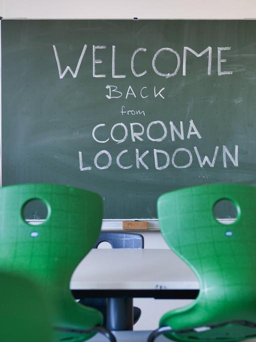Ein leeres Klassenzimmer mit grünen Stühlen und einer Tafel, auf der steht: "Welcome Back From Corona Lockdown"-
