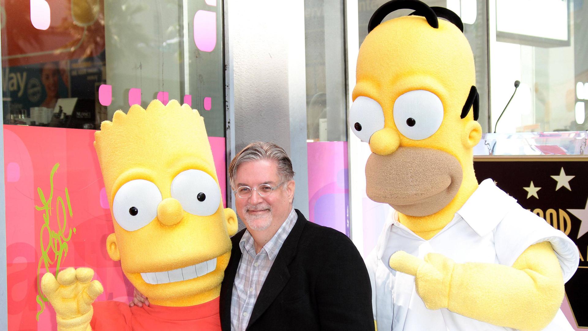 Simpsons-Erfinder Matt Groening (M.) mit den beiden Simpsons-Charakteren Bart (l.) und Homer (r.) im Jahr 2012 bei der Ehrung mit einem Stern auf dem Walk of Fame.