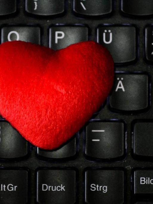Ein rotes Herz aus Stoff liegt auf der Tastatur eines Notebooks.