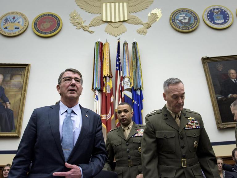 US-Verteidigungsminister Ashton Carter und Generalstabschef Joseph Dunford stehen in einem Raum, hinter ihnen sind weitere Personen und einige Fahnen zu sehen.