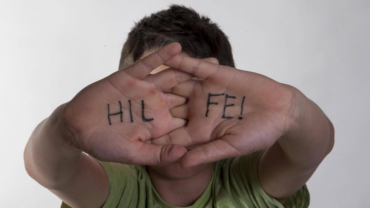 "Hilfe" steht auf den Händen, die ein Kind vor sein Gesicht hält.