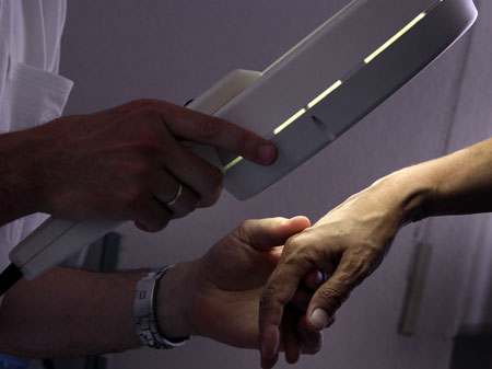 Ein Hautarzt untersucht mit einem Vergrößerungsglas die Haut einer Patientin bei einer Hautkrebs-Früherkennung