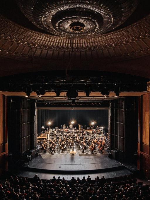 Das Orchester ist im imposanten Theaterraum der Volksbühne zu sehen.