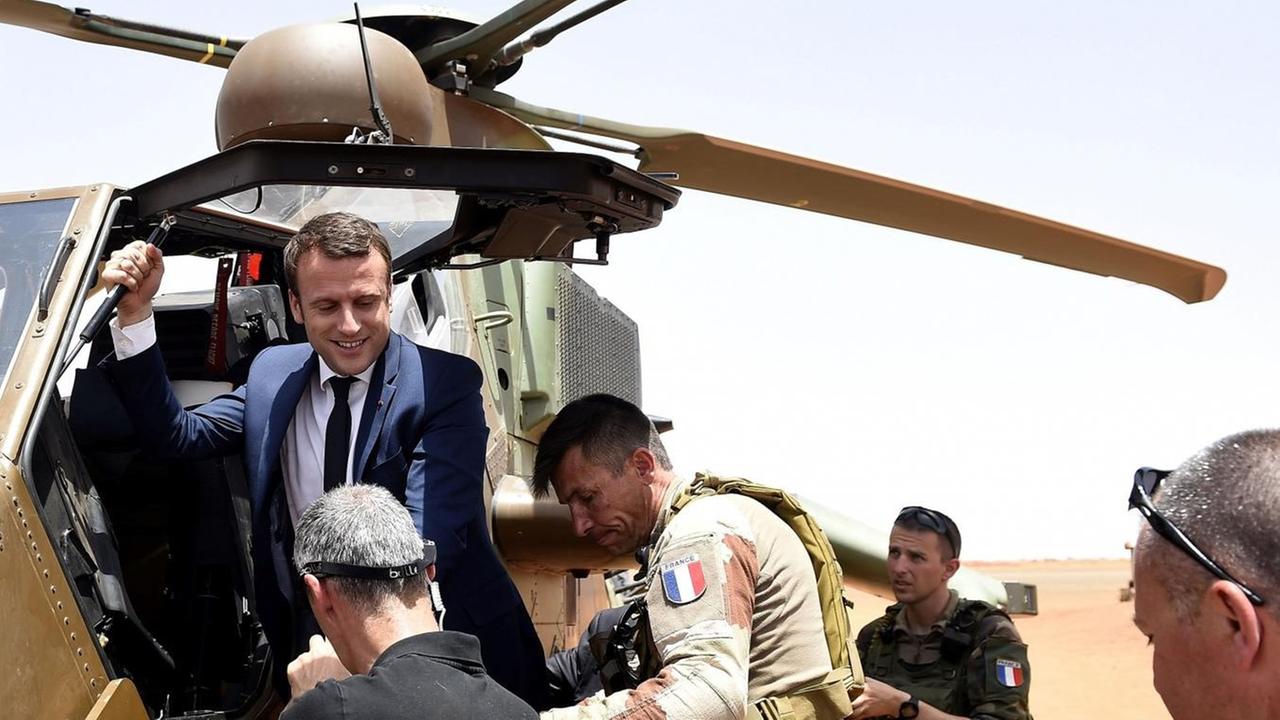 Macron steigt in einem Wüstengebiet aus einem Hubschrauber, mehrere Person stehen drumherum.