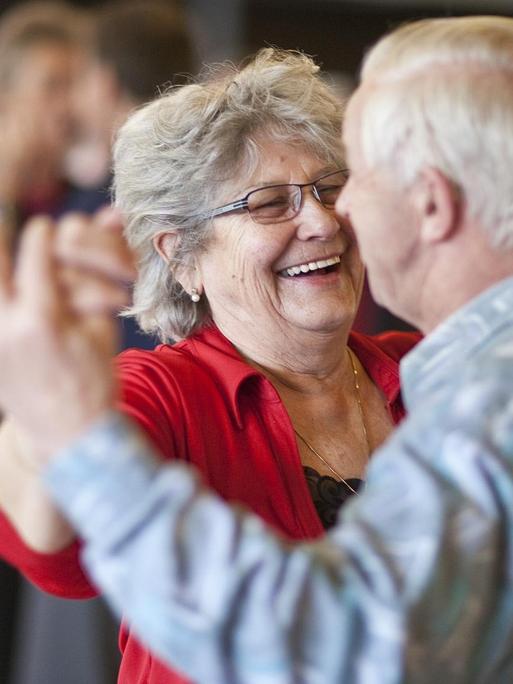 Ein Seniorenpaar tanzt lachend miteinander.