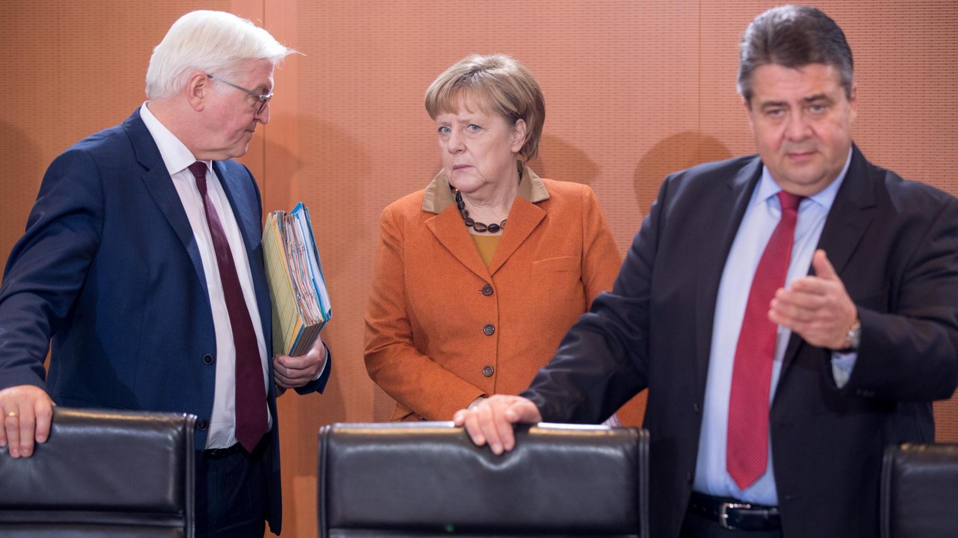 Bundesaußenminister Frank-Walter Steinmeier (SPD), Bundeskanzlerin Angela Merkel (CDU) und Bundeswirtschaftsminister Sigmar Gabriel (SPD) (v.l.) stehen am Kabinettstisch.