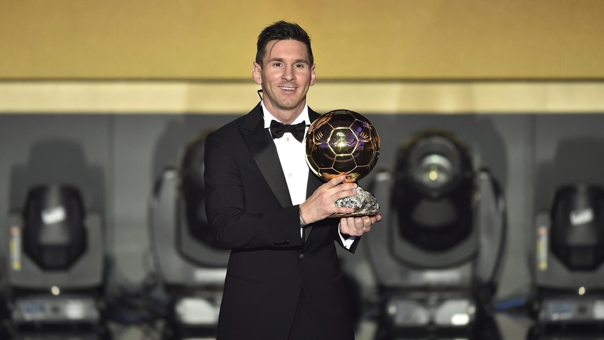 Der Fußballer Lionel Messi steht bei der Gala zum Weltfußballer des Jahres im schwarzen Anzug auf der BÜhne und hält lachend seine Auszeichnung in den Händen.