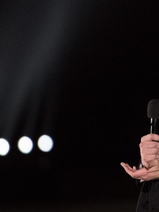 Elon Musk bei einer Rede in Texas, er steht vor dunklem Hintergrund und hält ein Mikrofon in der Hand.