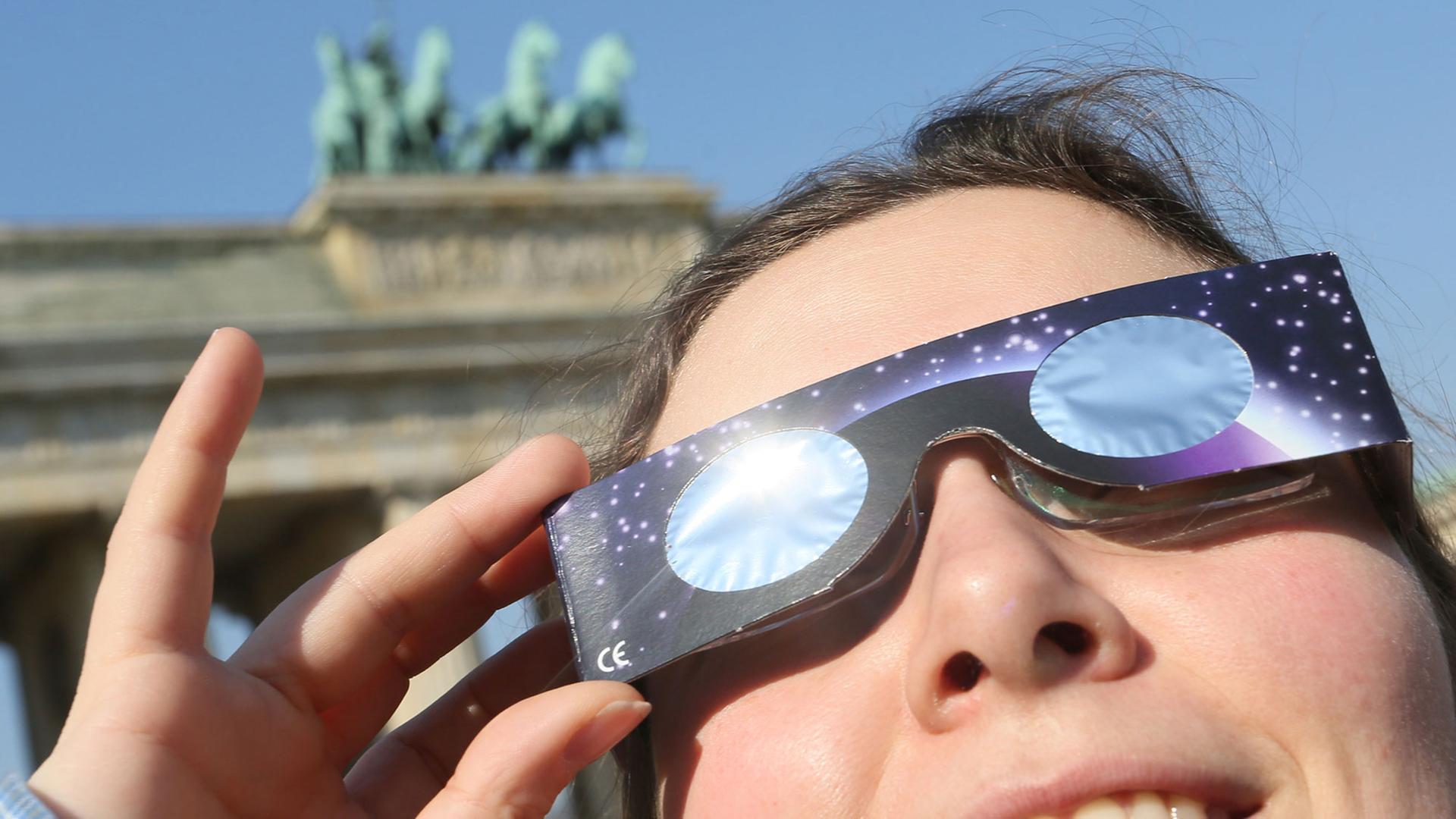 Eine junge Frau beobachtet die Sonnenfinsternis durch eine Schutzbrille