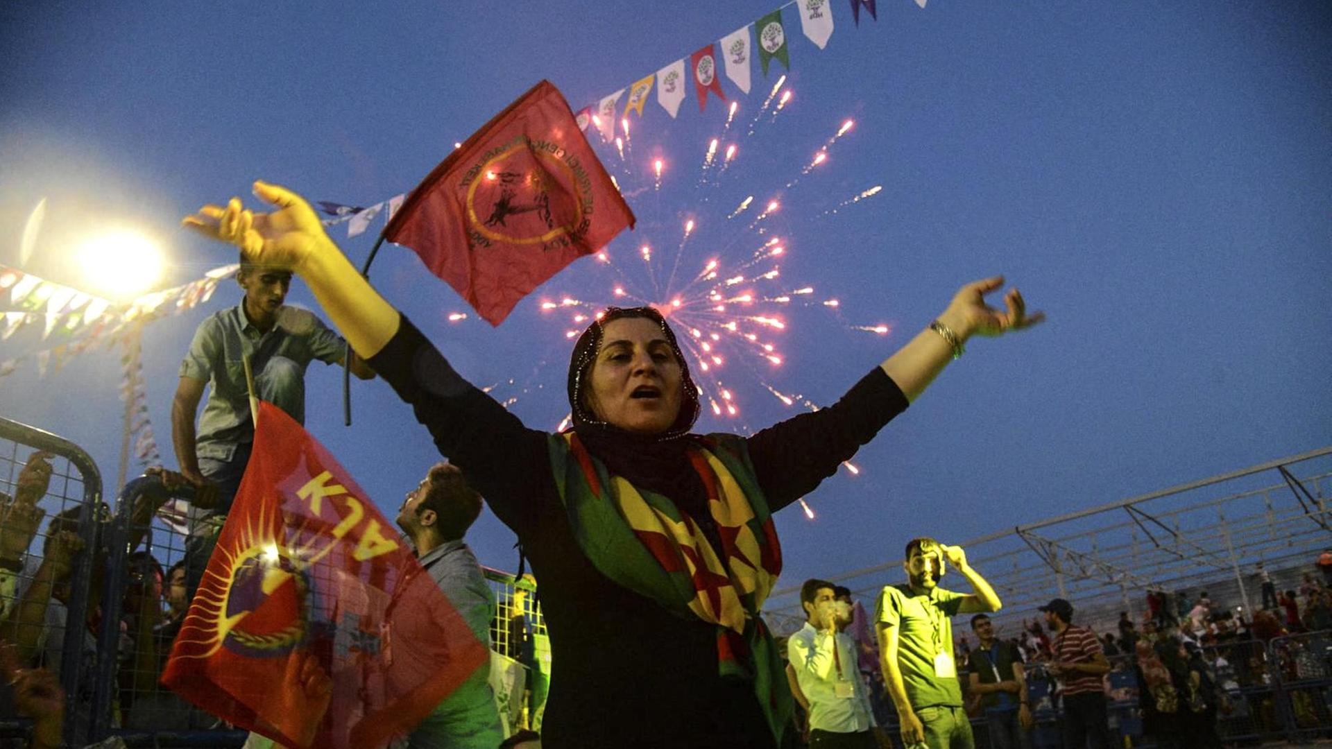 Eine Frau reißt die Arme in die Luft. Im Hintergrund Fahnen und Feuerwerk.