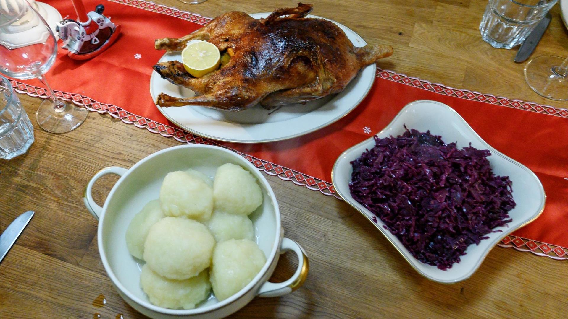 Eine gebratene Ente sowie Klöße und Rotkohl stehen auf einem gedeckten Tisch.