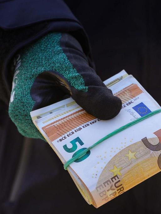 Ein Zollbeamter hält ein Bündel Geldscheine in der Hand.
