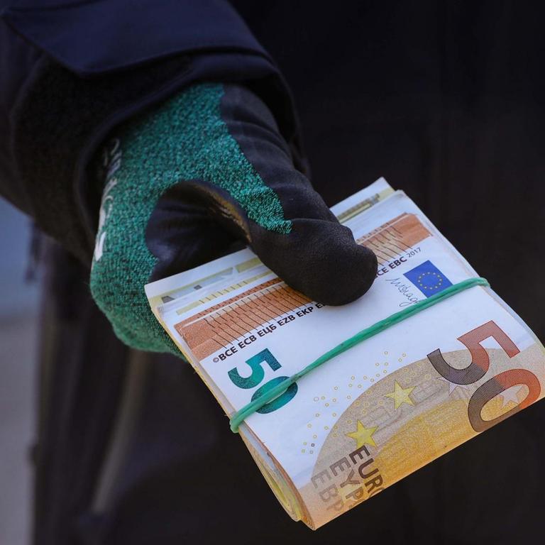 Ein Zollbeamter hält ein Bündel Geldscheine in der Hand.