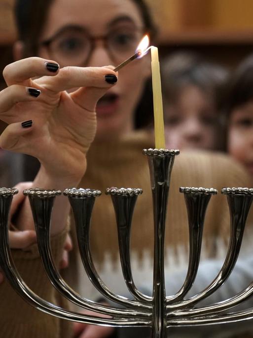Eine Gruppe von Kindern und einer Frau zünden eine Chanukkah Kerze zum jüdischen Lichterfest am neunarmigen Leuchter an.