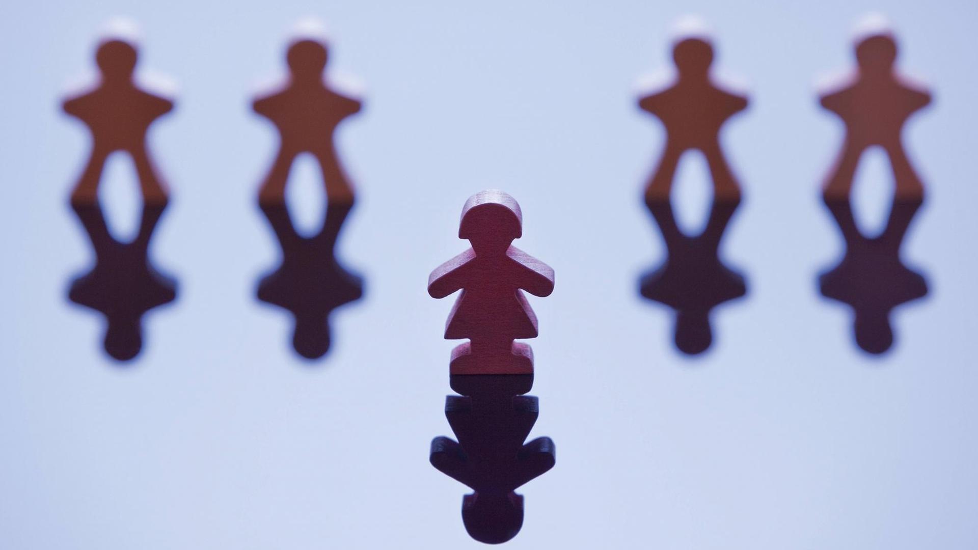 Vier männlich wirkende Spielfiguren stehen in einer Reihe mit einer Lücke in der Mitte, davor steht eine weiblich wirkende Figur.