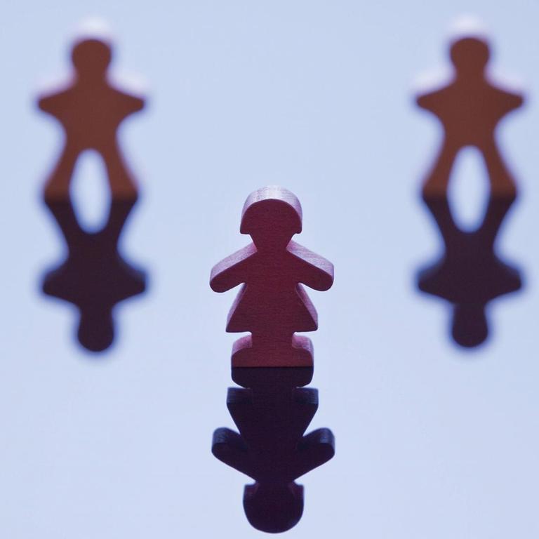 Vier männlich wirkende Spielfiguren stehen in einer Reihe mit einer Lücke in der Mitte, davor steht eine weiblich wirkende Figur.