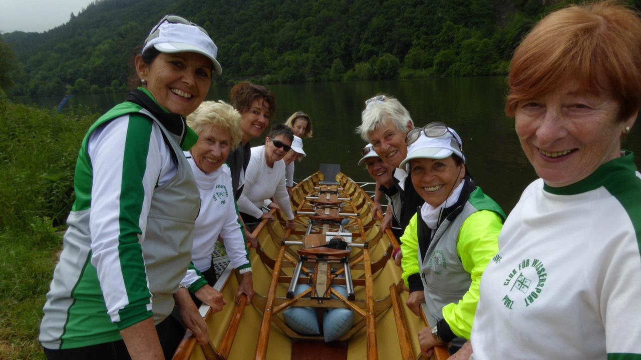 Frauen tragen ein Boot, im Hintergrund die Mosel. 