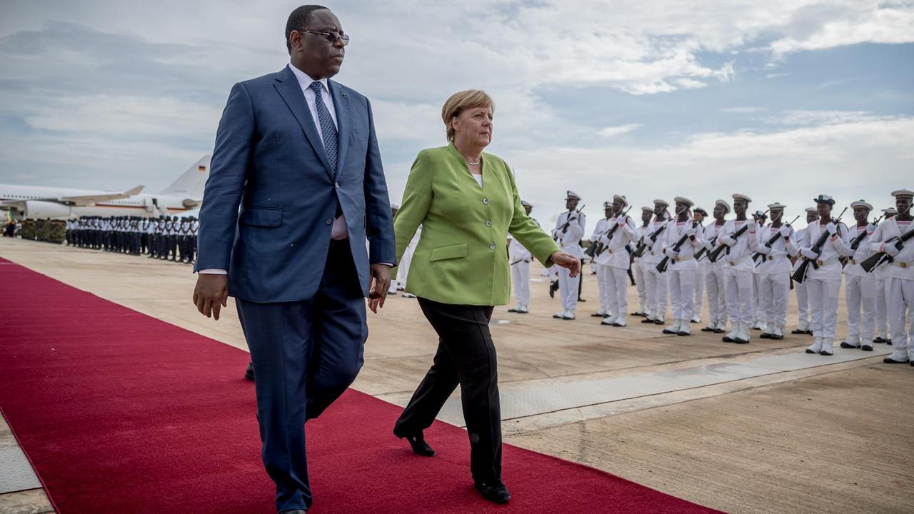 Angela Merkel und Macky Sall gehen nebeneinander auf einem roten Teppich.