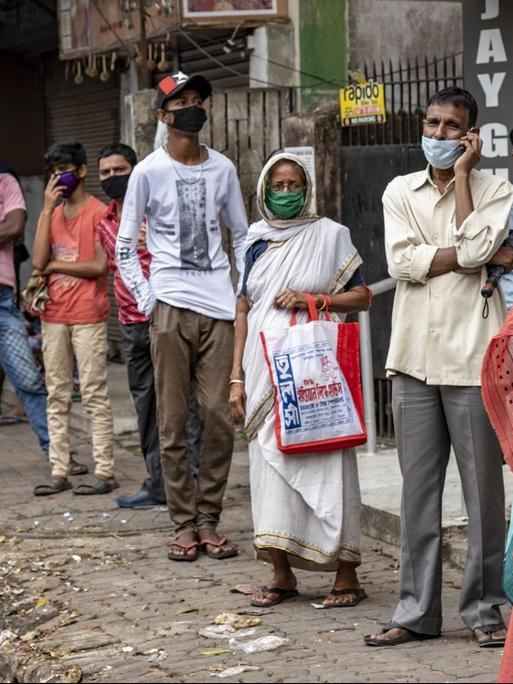 Menschen in Kalkutta stehen in einer Reihe und warten auf Essen, das von einer NGO ausgeteilt wird.
