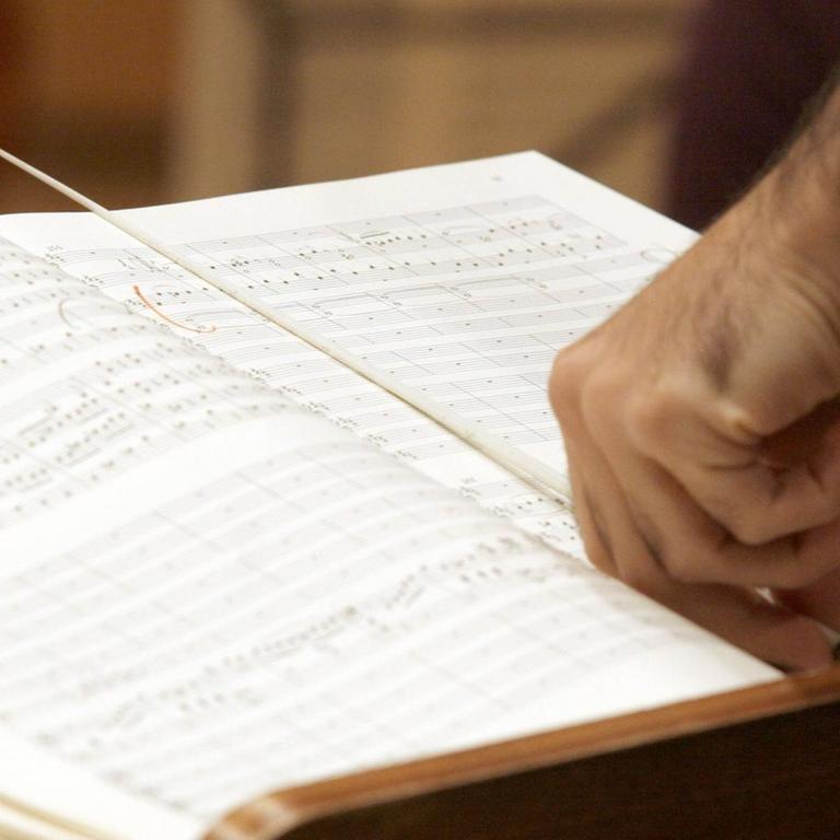 Ein Dirigent steht mit einem Taktstock vor seinem Pult und schaut in die Notenblätter