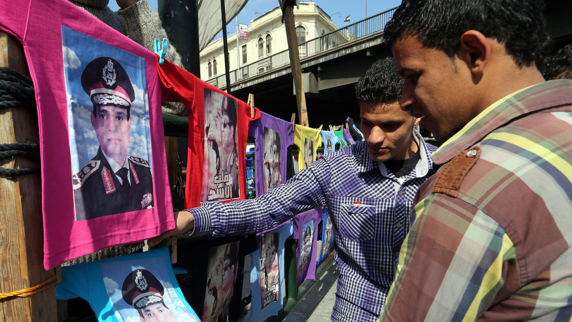 Zwei ägyptische Männer betrachten T-Shirts mit dem Bild von Abdel Fattah al Sisi.