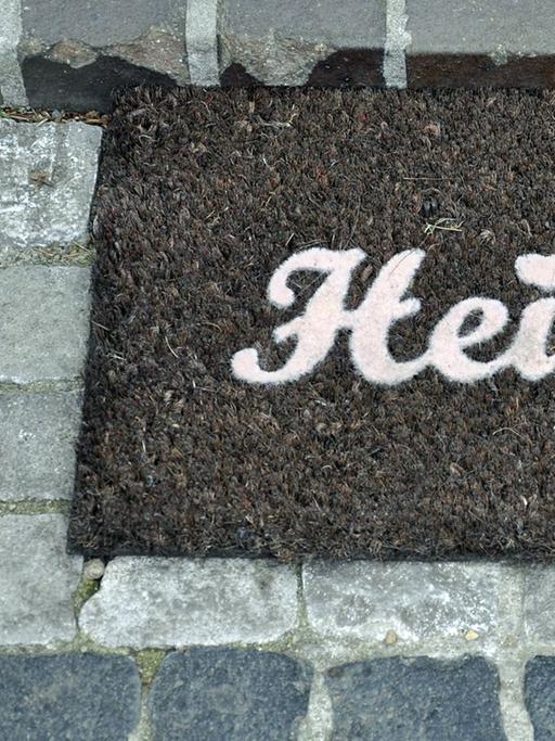 Ein Fußabtreter mit dem Schriftzug "Heimat"liegt auf einem gepflasterten Weg.
