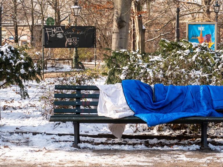Ein Schlafsack liegt auf einer Bank im winterlichen Berlin. Im Großen Tiergarten liegt Schnee.