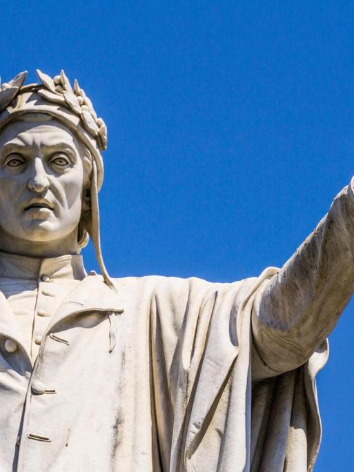 Die Dante-Alighieri-Skulptur in Neape vor blauem Himmel. Der Dichter streckt die linke Hand auf Schulterhöhe aus.