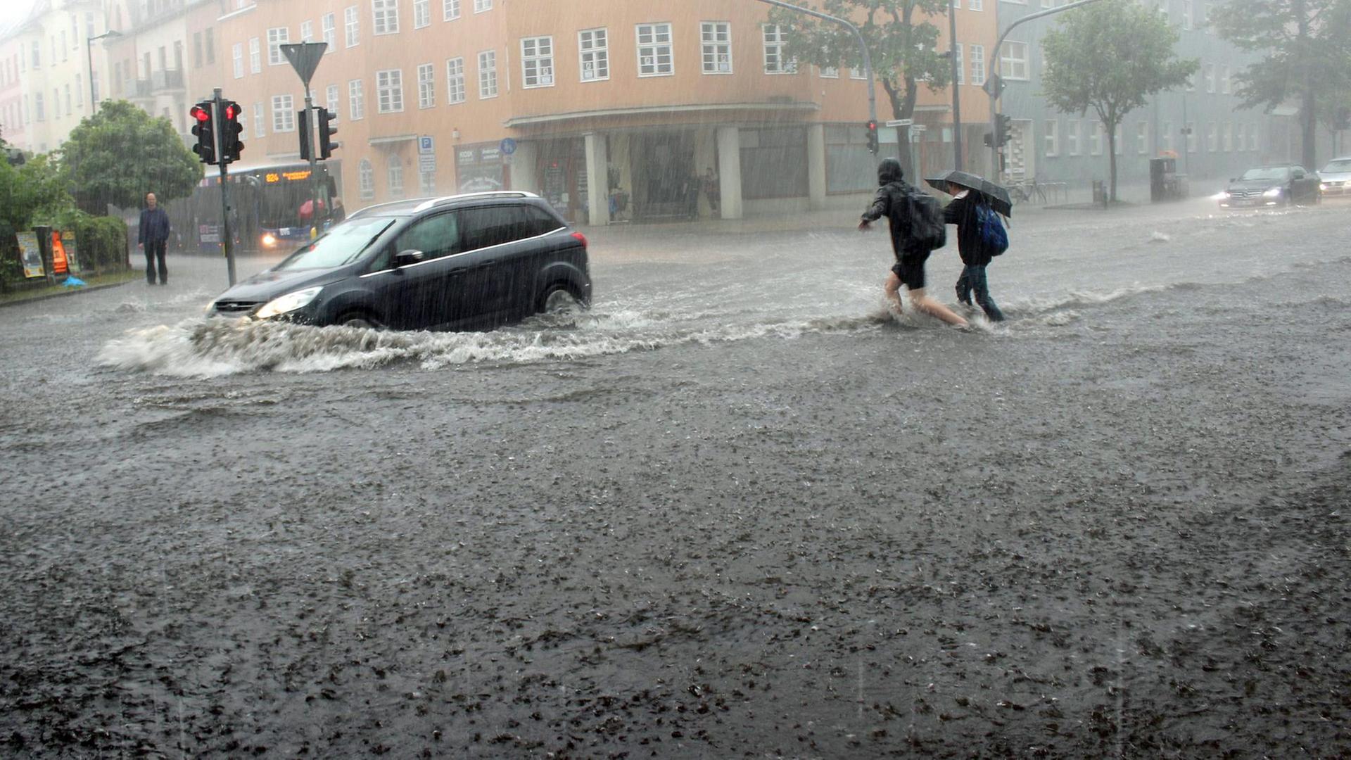 Ein Auto fährt in Oranienburg in Brandenburg über eine nach Starkregen völlig überflutete Kreuzung während Fußgänger durch das Wasser waten, aufgenommen 2017.