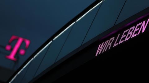 Das T-Logo der Deutschen Telekom vor dunklem Himmel. Dazu die Worte "Wir leben".