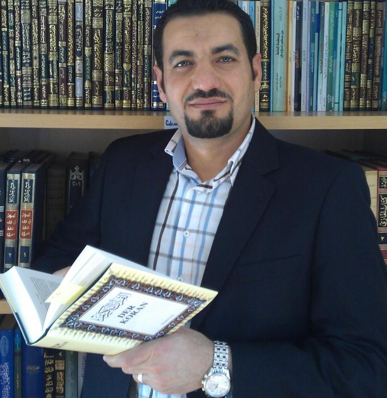 Mahmoud Abdallah mit einer aufgeschlagenen Koran-Übersetzung in der Hand vor einem Bücherregal mit arabischen Büchern.