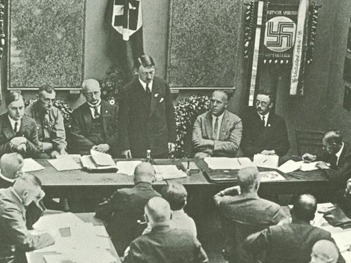 Hitler in Munich adressing a meeting of the NSDAP in 1925. Third to the left of Hitler is Alfred Rosenberg, on the right are Gregor Strasser and Heinrich Himmler. Far right by the door is Julius Streicher. | Verwendung weltweit, Keine Weitergabe an Wiederverkäufer.