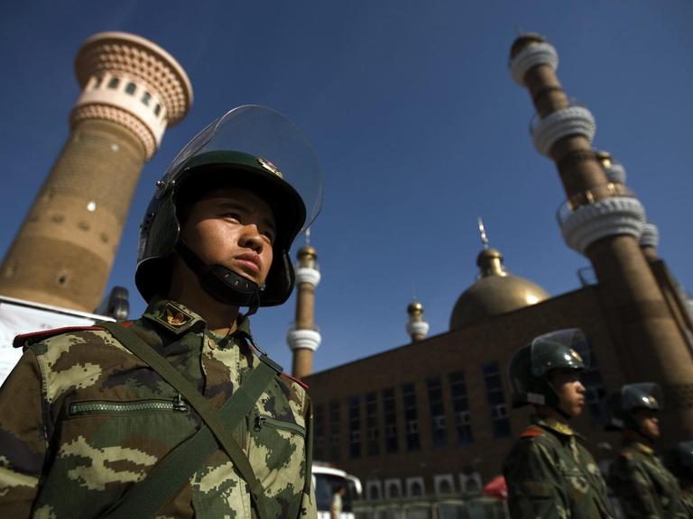Aus einer Untersicht sind uniformierte und bewaffnete Sicherheitskräfte zu sehen, die vor einer Mosche patrouillieren.