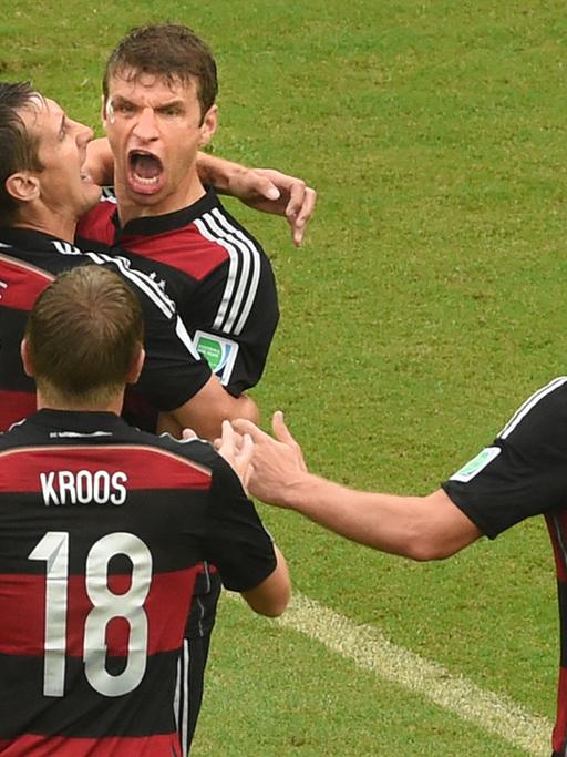 Miroslav Klose fällt Thomas Müller um den Hals, der siegreiche eine Faust macht; Toni Kroos und Benedikt Höwedes laufen auf die beiden zu.